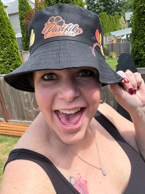 Woman wearing black Pasifika Grill & Bar bucket hat with hibiscus accents